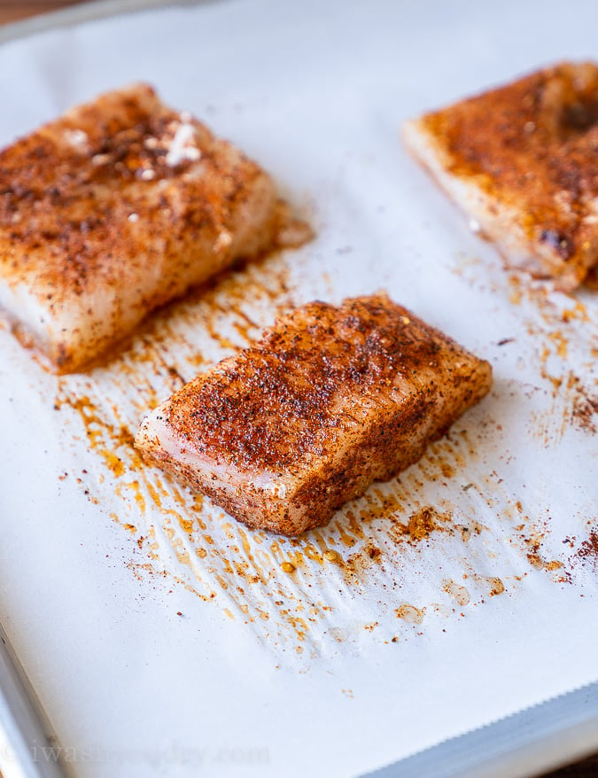 Seasoned fish filets on a baking sheet just before being baked.