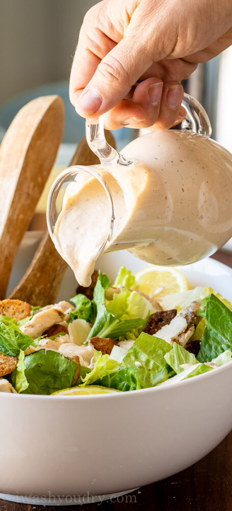 Homemade Caesar Salad Dressing being poured over chopped lettuce.