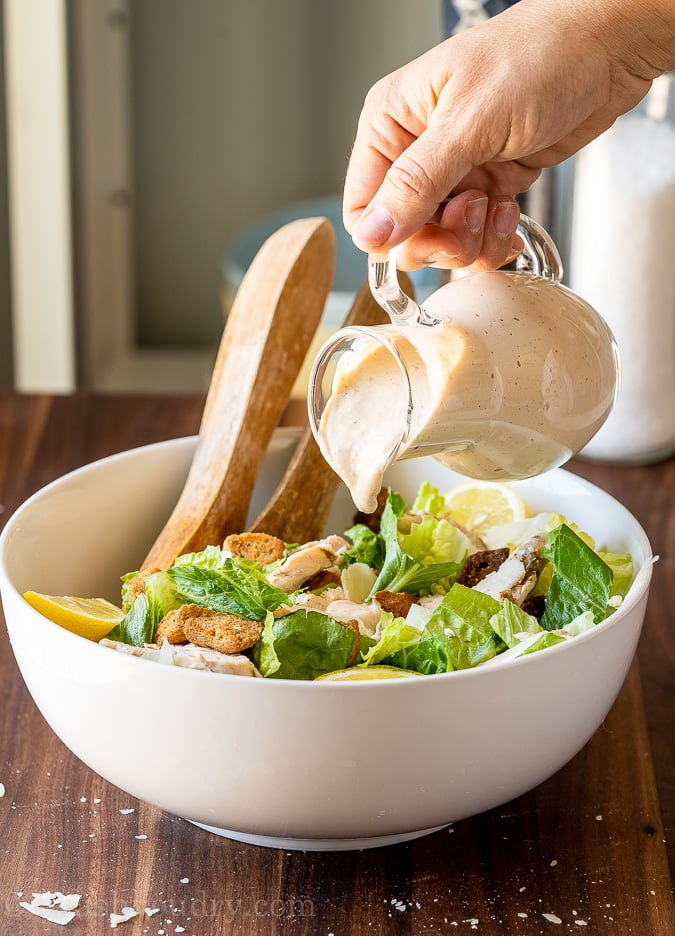 Homemade Caesar Salad Dressing being poured over chopped lettuce.