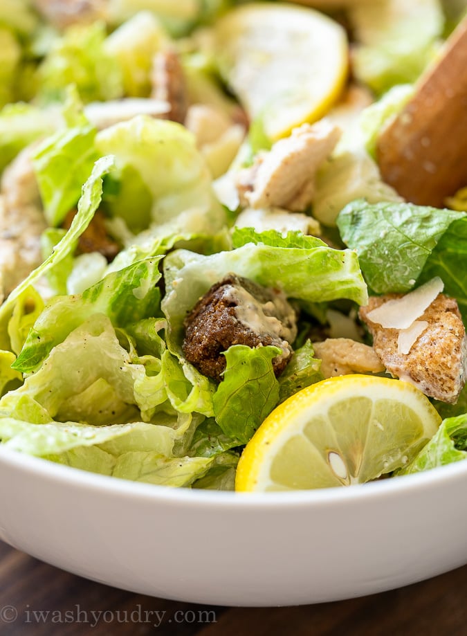 Bowl of crisp romaine lettuce and crunchy croutons and Caesar salad dressing on top