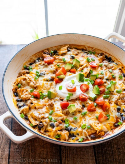 Skillet full of Chicken Black Bean Enchiladas, topped with sour cream, diced tomatoes and avocado!
