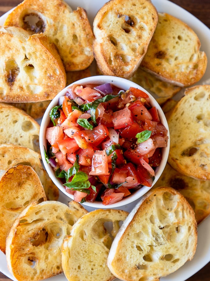 Small white bowl filled with tomato salad and toasted bread slices all around.