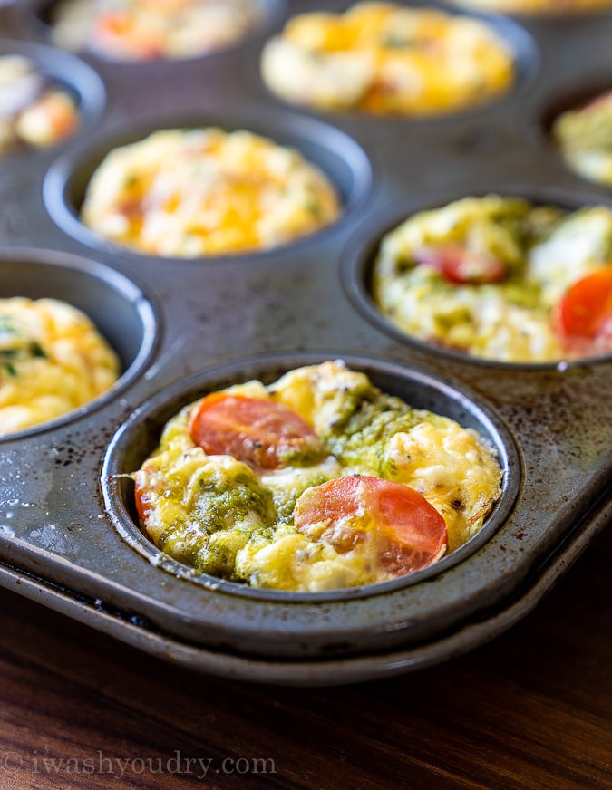 Close up image of mini frittata in muffin tin. Topped with tomatoes and basil pesto sauce.
