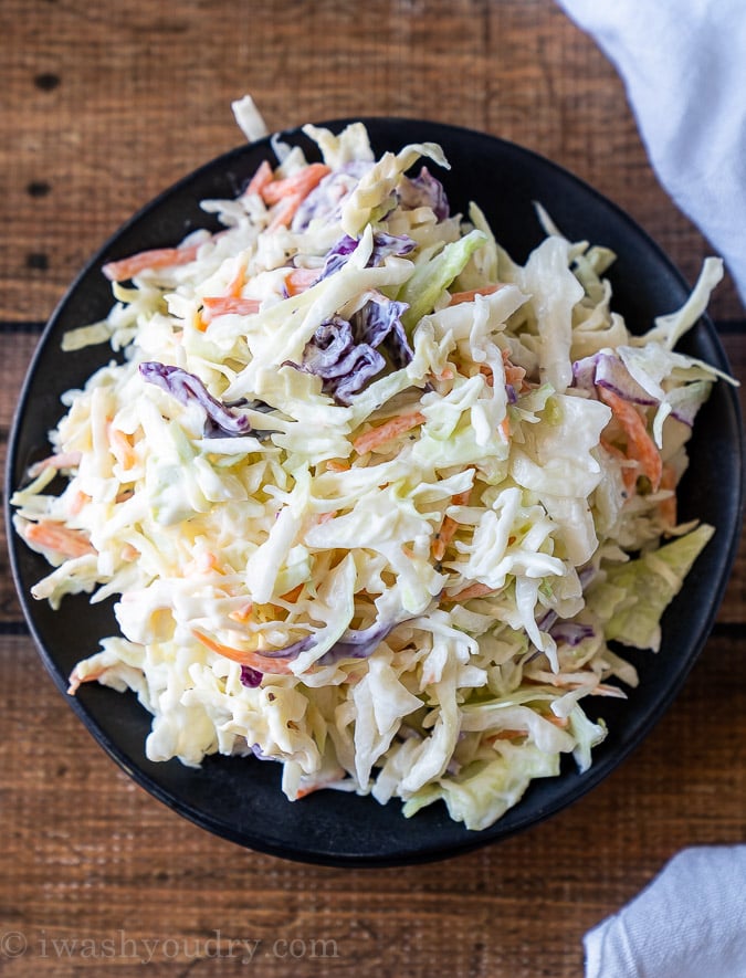 Top down picture of a black plate with coleslaw salad piled high.