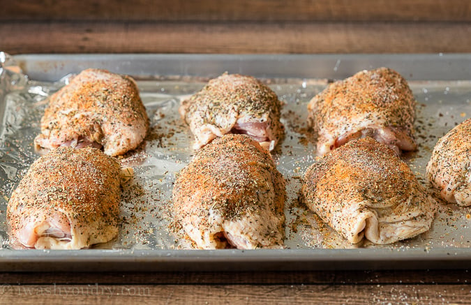 Uncooked chicken thighs on a lined baking sheet ready to go into the oven.