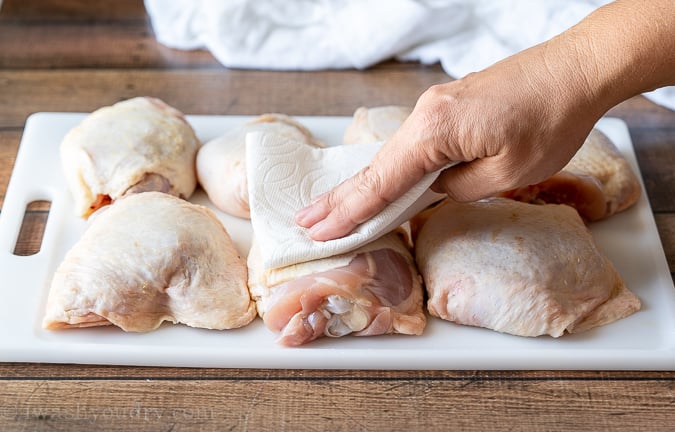 Using paper towels to pat dry the skin of chicken thighs to get a crispy baked chicken thigh. 
