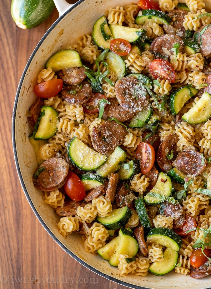 Skillet filled with pasta, sausages, zucchini and tomatoes in a lemon basil sauce.