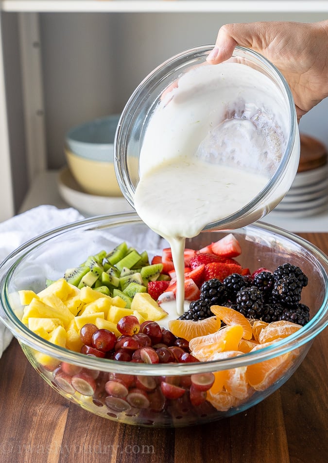 Creamy fruit salad dressing pouring over fresh fruits