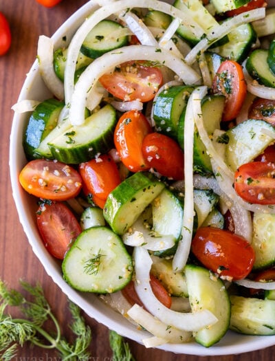 White bowl filled with cool cucumbers, tomatoes and sliced onions