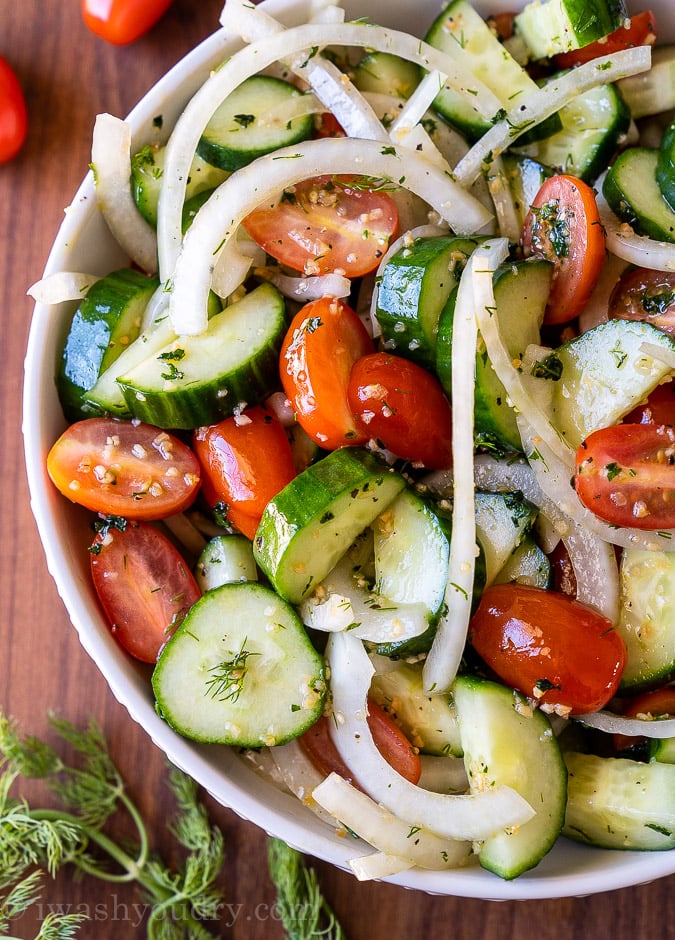 White bowl filled with cool cucumbers, tomatoes and sliced onions