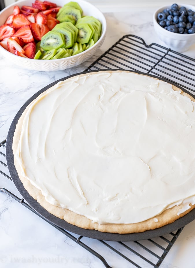 Cream cheese frosting on top of fruit pizza dough.