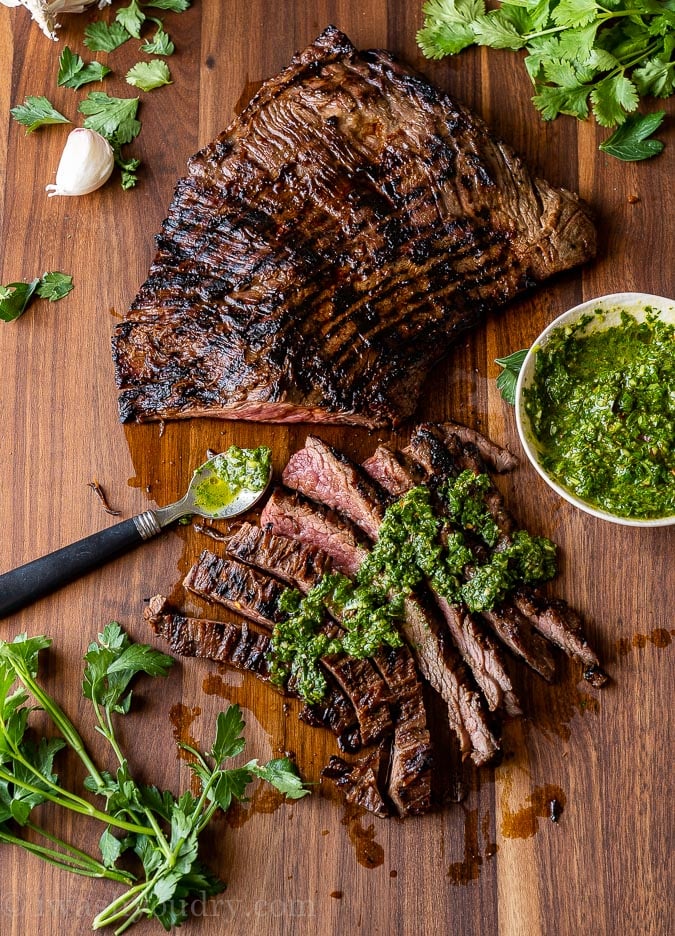 Grilled and sliced skirt steak on a cutting board with chimichurri sauce on top.