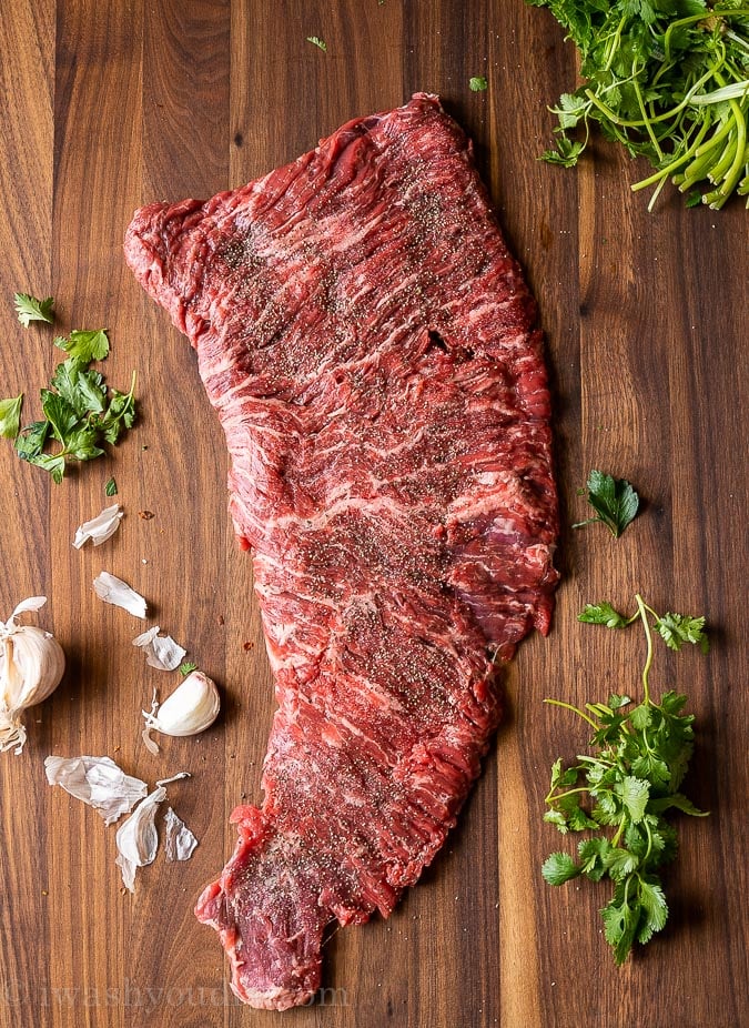 Skirt steak on a cutting board, uncooked so you can see the fibers running through the cut of beef.