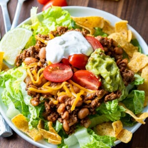 This Quick Taco Salad Recipe is filled with seasoned ground beef and pinto beans on top of corn chips and lettuce with all your favorite taco toppings. It's great for busy weeknights!