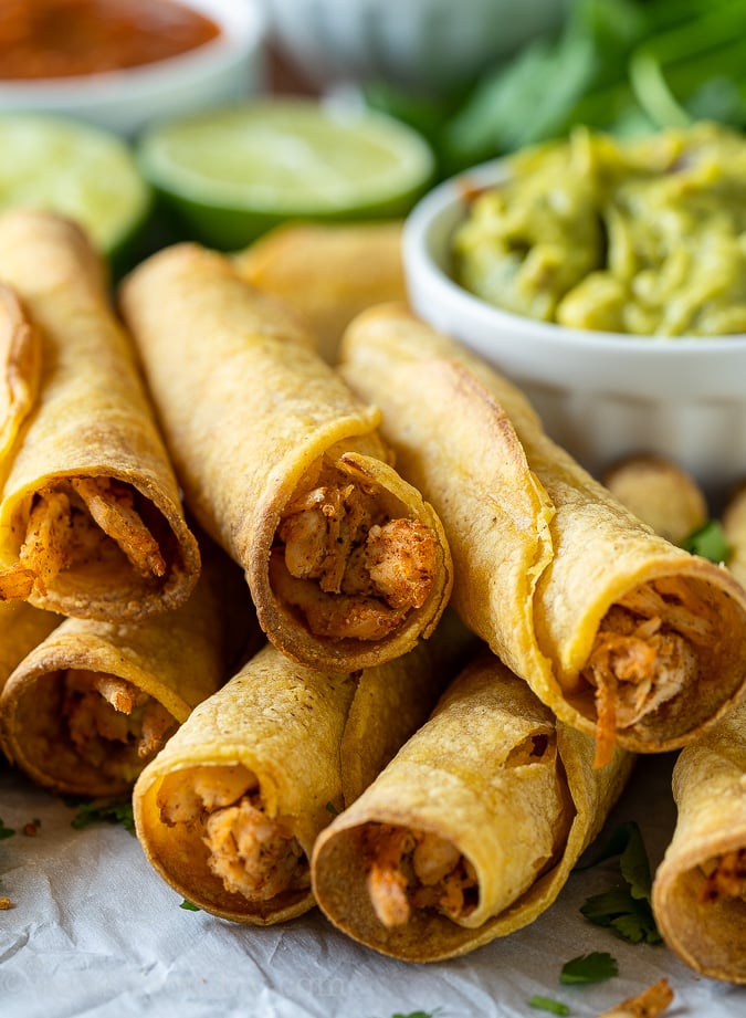 Stack of crispy baked chicken taquitos next to guacamole.