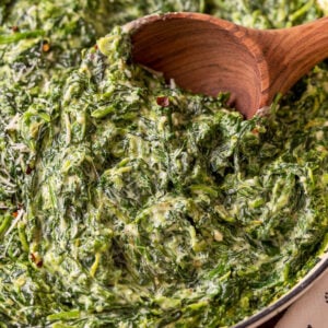 closeup of spinach in a pan with wooden spoon