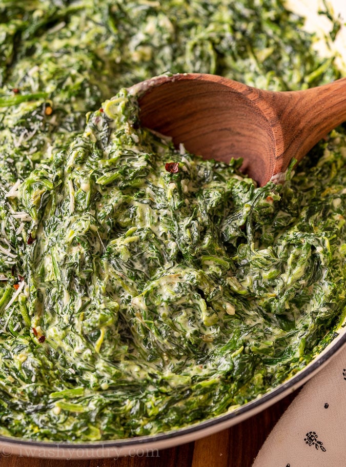 closeup of spinach in a pan with wooden spoon