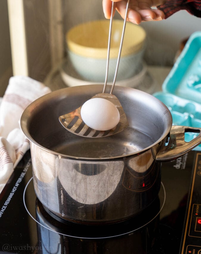 lowering egg into pot of water with spoon