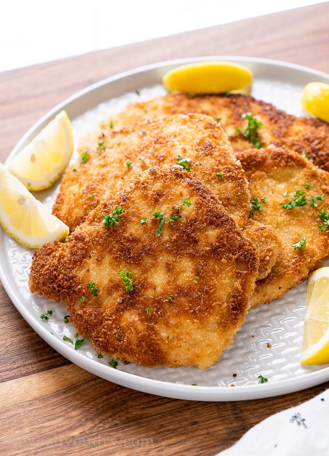 breaded pork cutlets one a platter with lemon wedges.