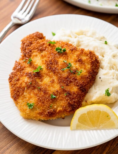 pork schnitzel on top of mashed potatoes with lemon wedge.