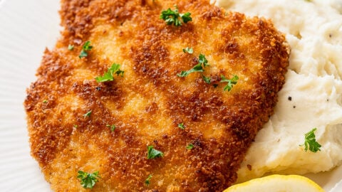 pork schnitzel on top of mashed potatoes with lemon wedge.