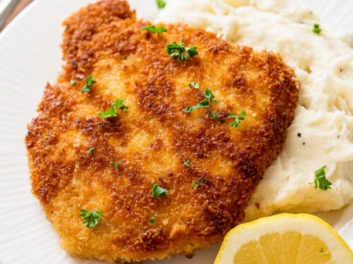 pork schnitzel on top of mashed potatoes with lemon wedge.