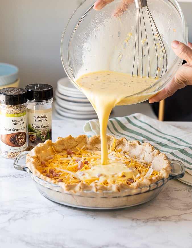pouring egg filling into pie crust to bake quiche