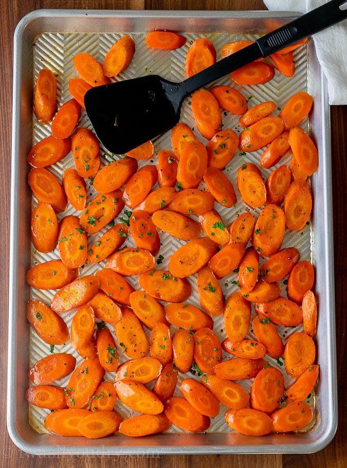sheet pan with sliced and roasted carrots and black spatula.