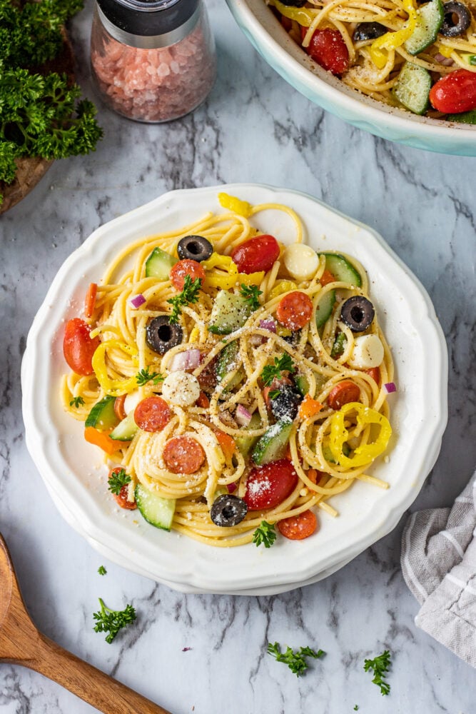 overhead image of spaghetti salad on white plate with salt and parsley on a marble table. 