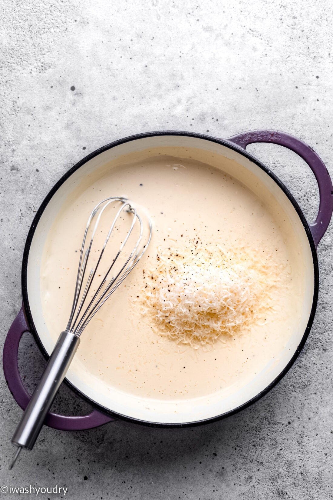 whisk in pot with creamy alfredo sauce and parmesan cheese.