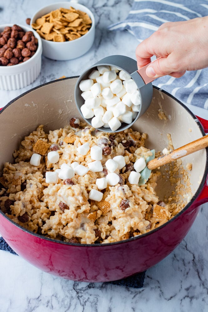 Pouring marshmallows into s'mores rice krispie treats mixture in a red pot. 