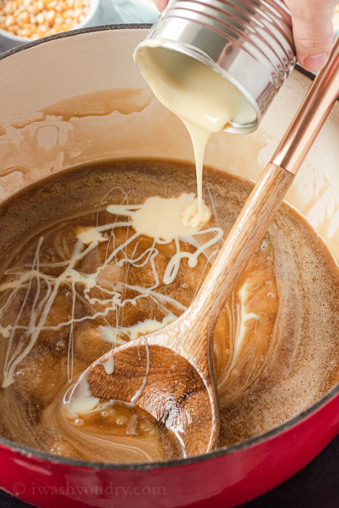 Pouring sweetened condensed milk into melted butter and brown sugar with wooden spoon. 