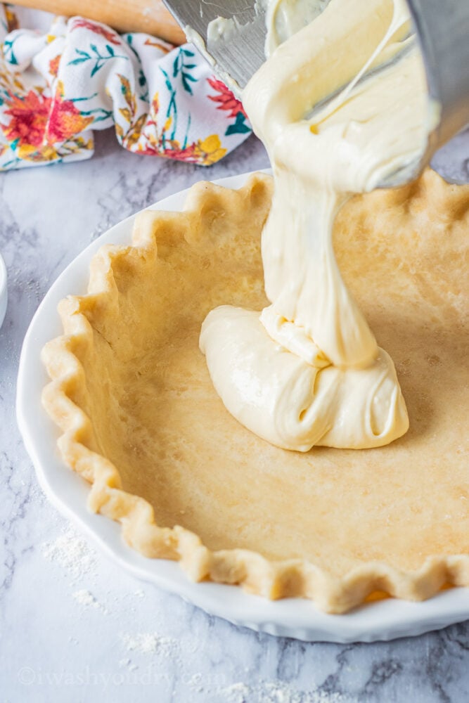 Pouring cheesecake filling into raw pie shell. 