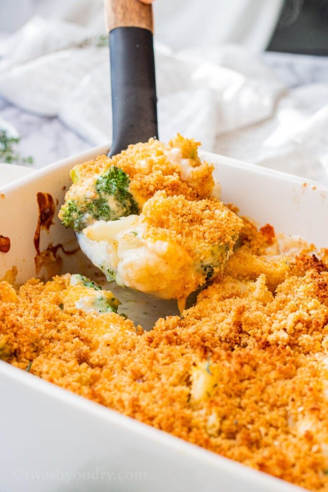 Spoonful of baked broccoli cauliflower casserole above white pan. 