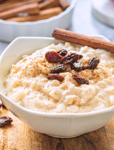 white bowl of cooked rice pudding and raisins on wood board.
