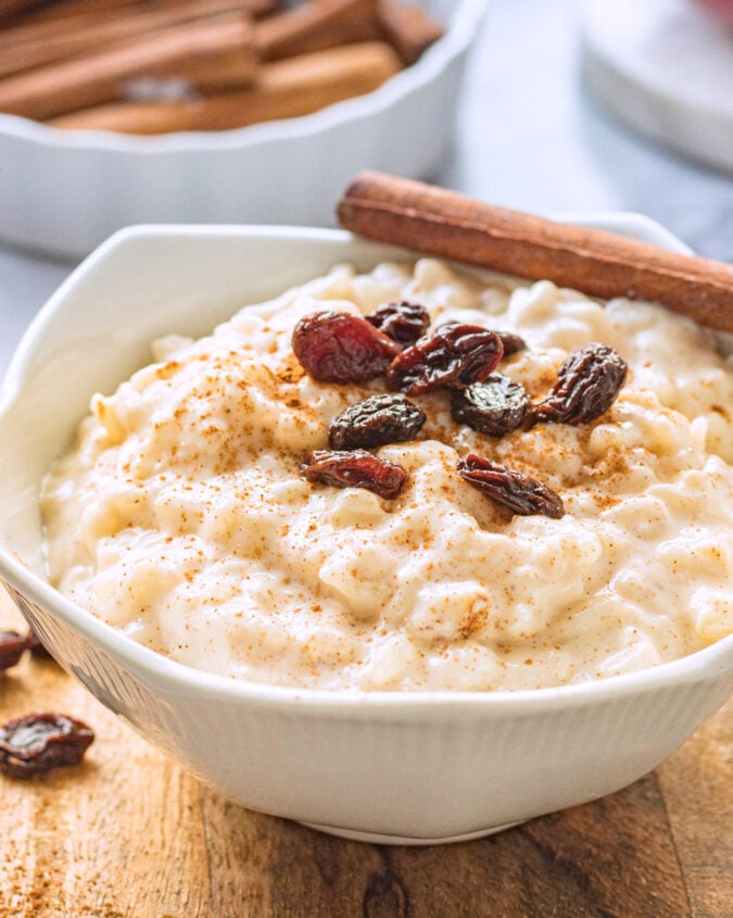 white bowl of cooked rice pudding and raisins on wood board. 