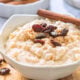 white bowl of cooked rice pudding and raisins on wood board.