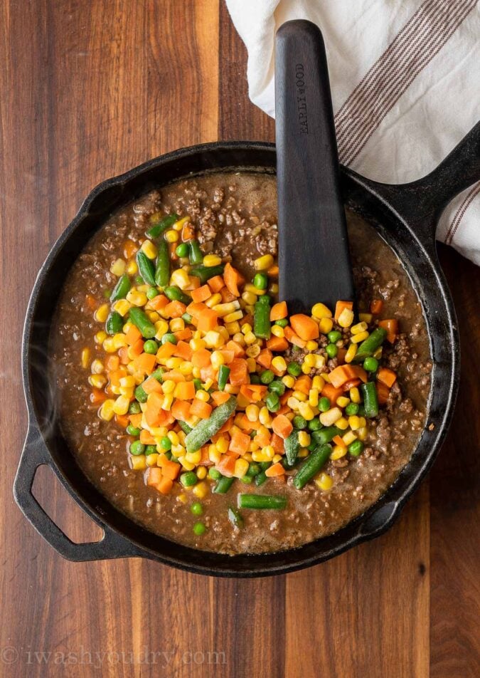 ground beef with brown gravy and mixed vegetables in black pan