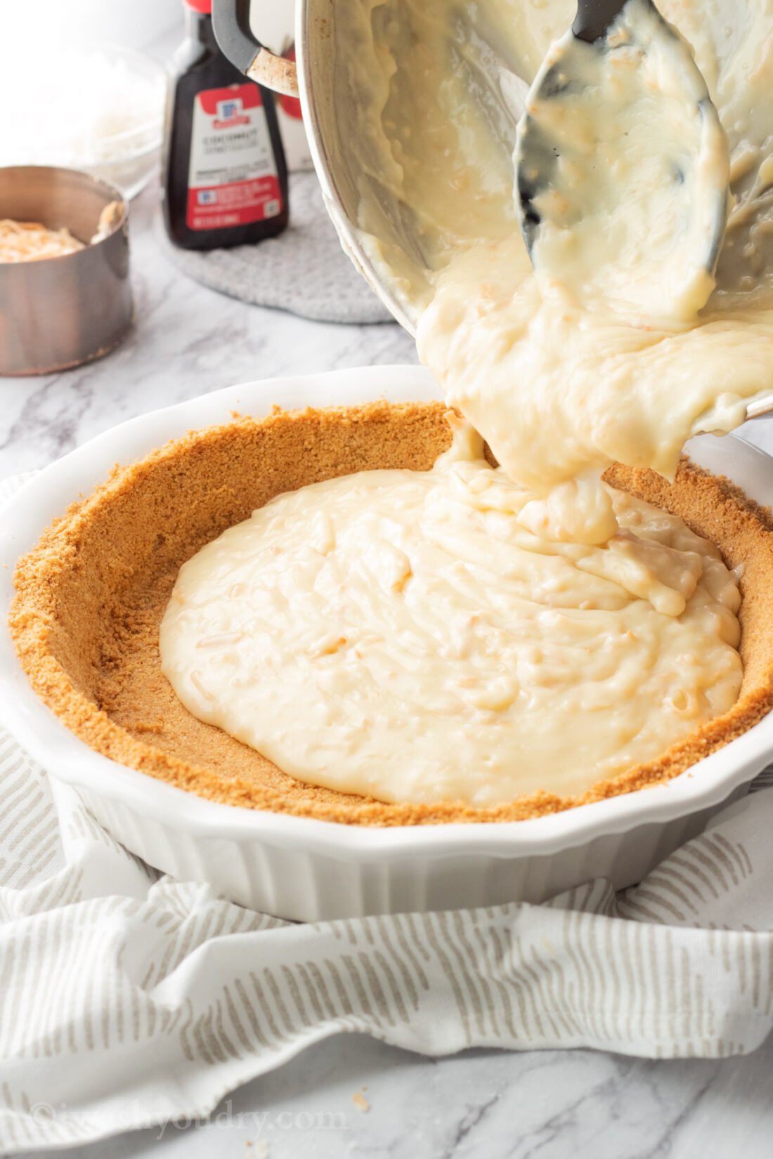 Pouring cooked coconut pudding into pie shell. 