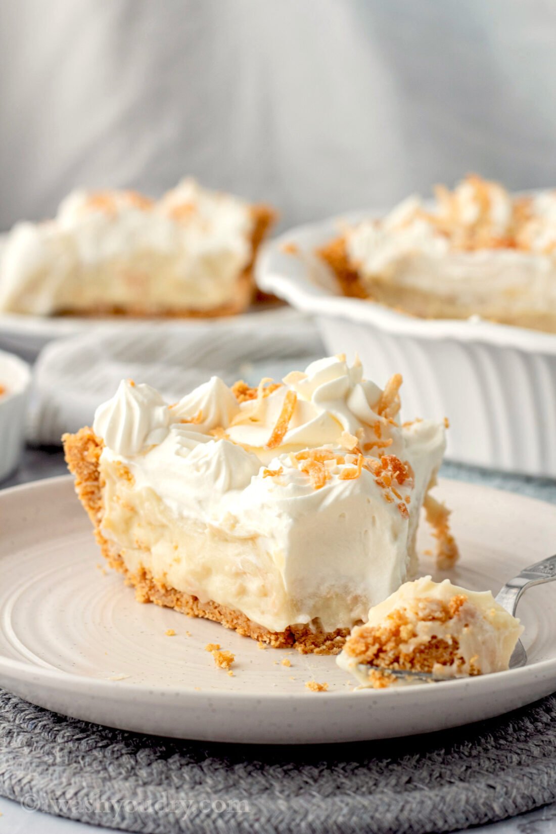 Slice of coconut cream pie with fork on white plate. 
