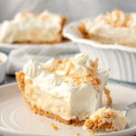 Slice of coconut cream pie in white plate with fork.