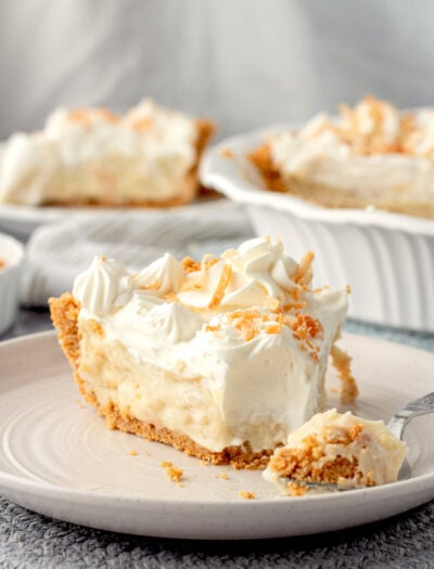 Slice of coconut cream pie in white plate with fork.