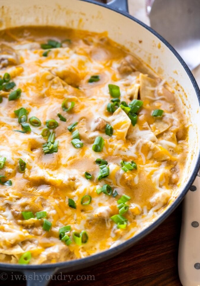 Skillet with cheesy chicken enchiladas and green onions