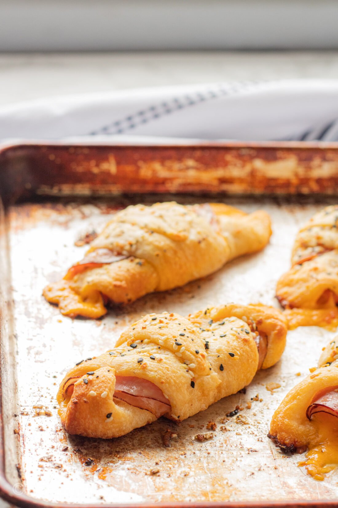 Baked Ham and Cheese Roll Ups in rows on metal pan. 