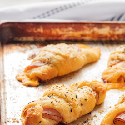 Baked Ham and Cheese Roll Ups in rows on metal pan.