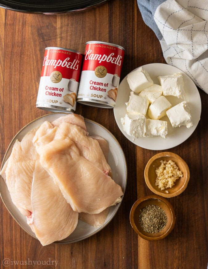 black slow cooker with chicken and cream cheese on top.