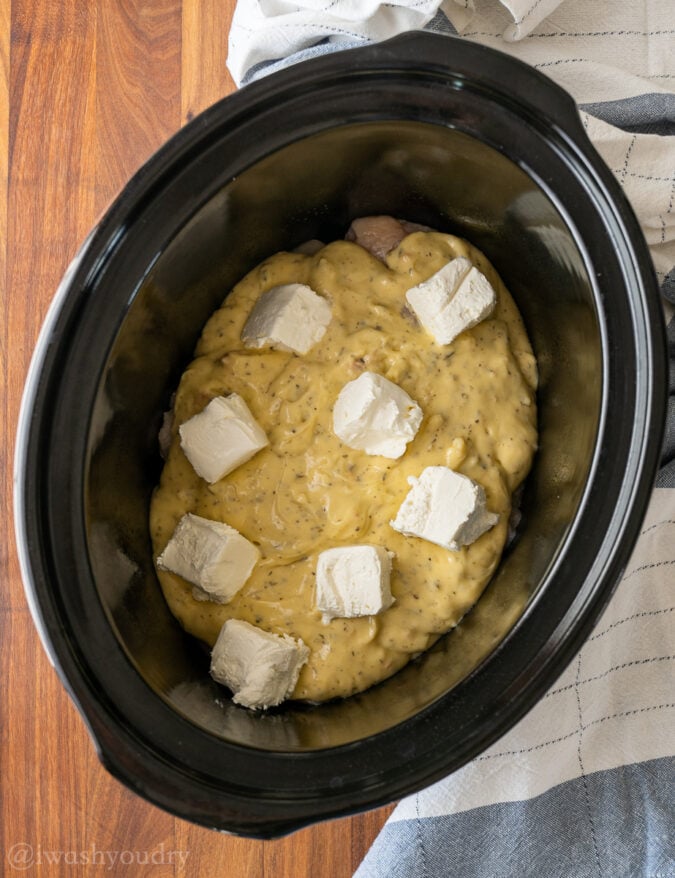black slow cooker with chicken and cream cheese on top.