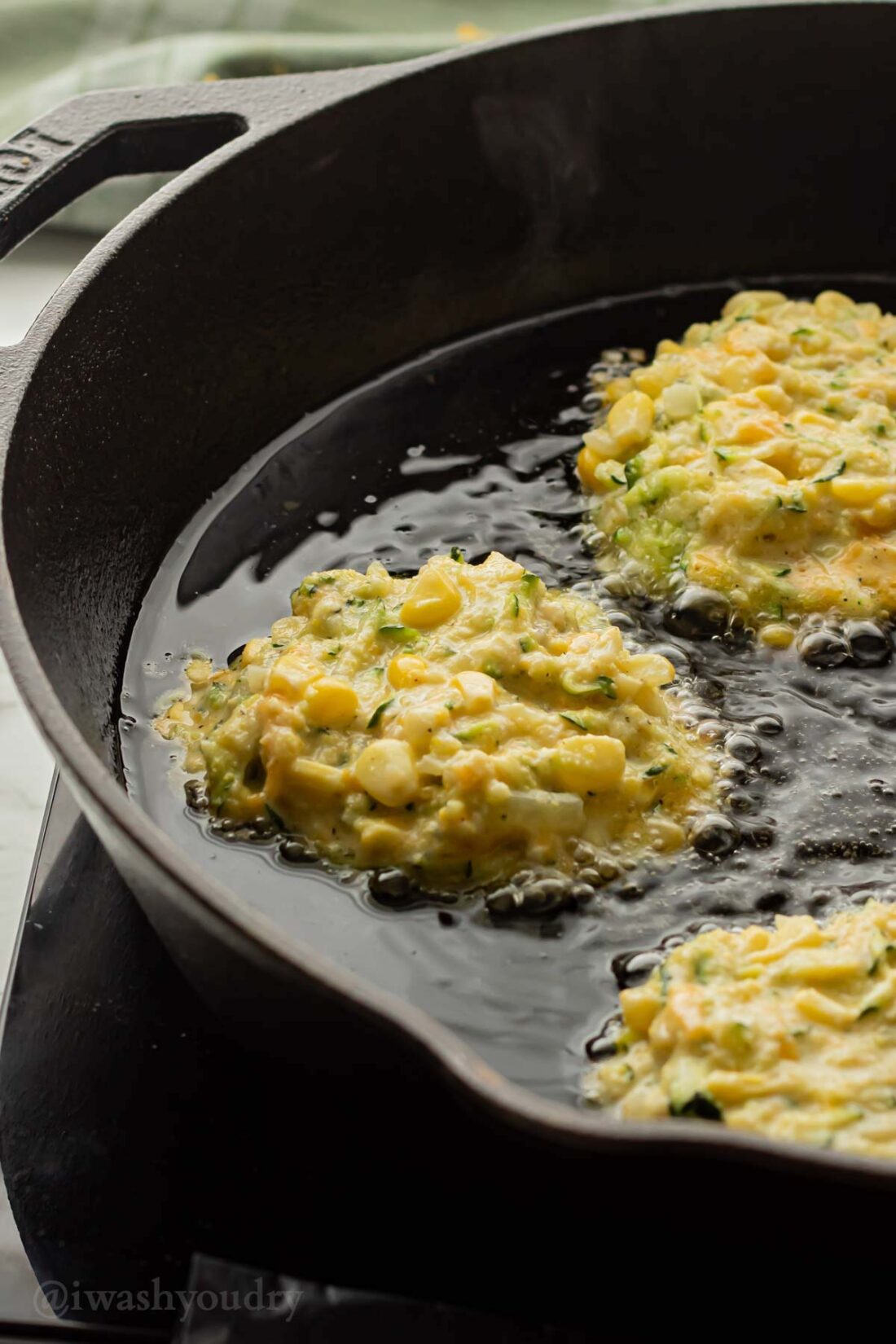 Corn fritter batter with raw zucchini in a black frying pan with oil. 