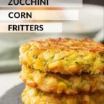 Stack of 3 cooked zucchini corn fritters on black slate.