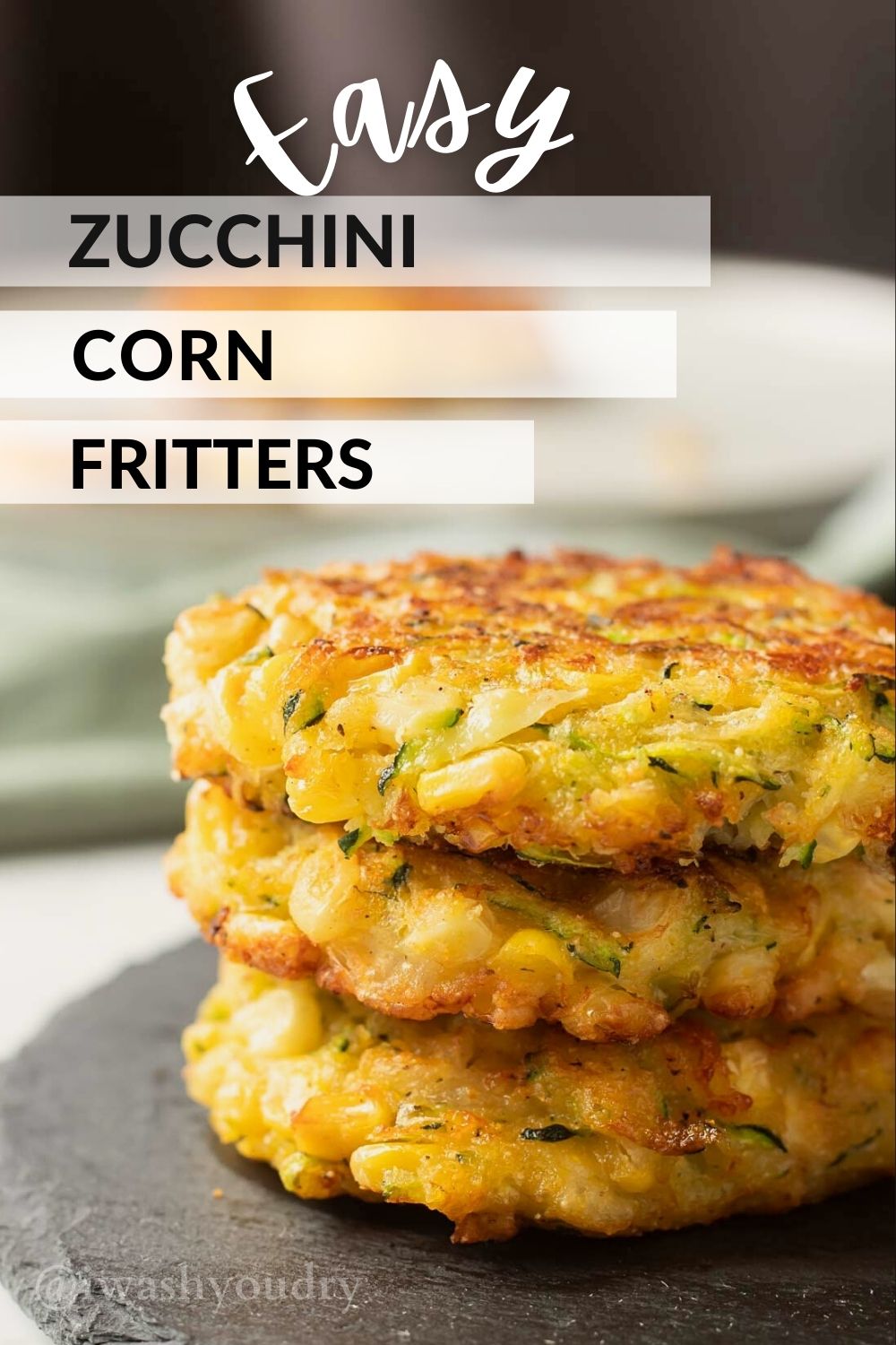 Stack of 3 cooked zucchini corn fritters on black slate. 
